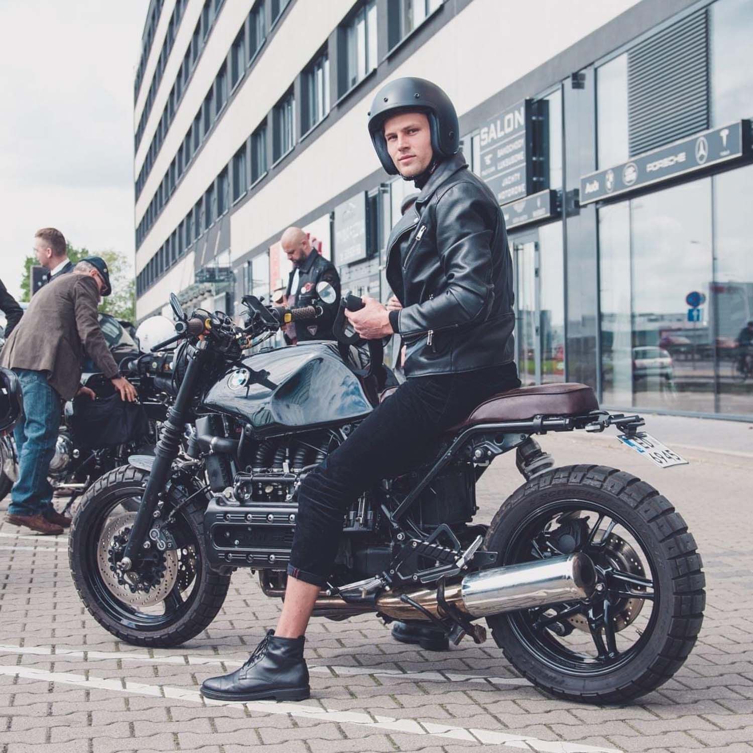 Rider in a leather jacket astride a BMW K-series brat on a Warsaw street
