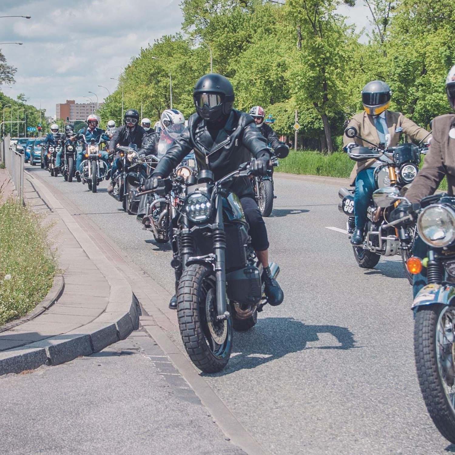 A pack of custom motorcycles riding two abreast down a tree-lined road