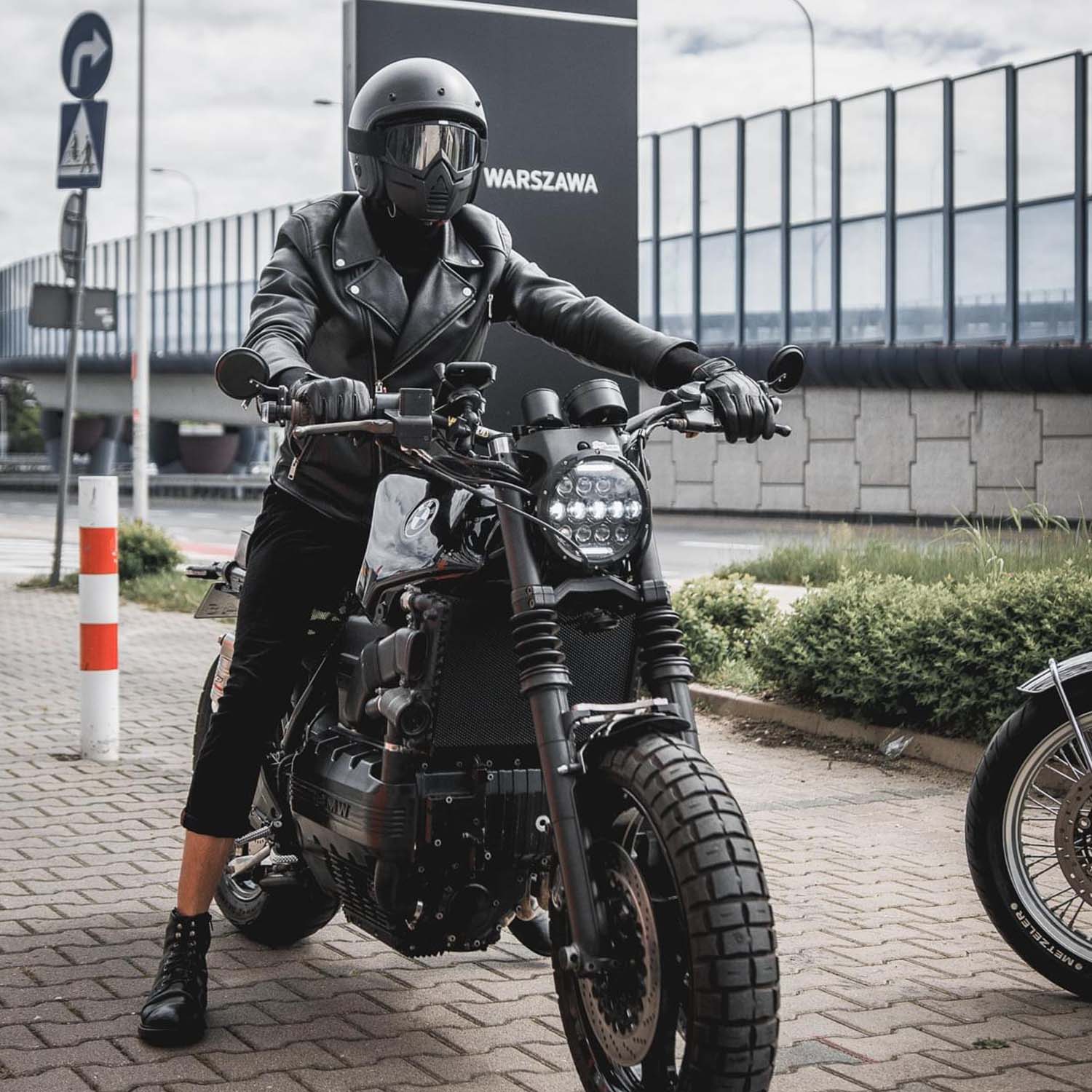 Helmeted rider on a BMW brat pulling away past a Warszawa road sign